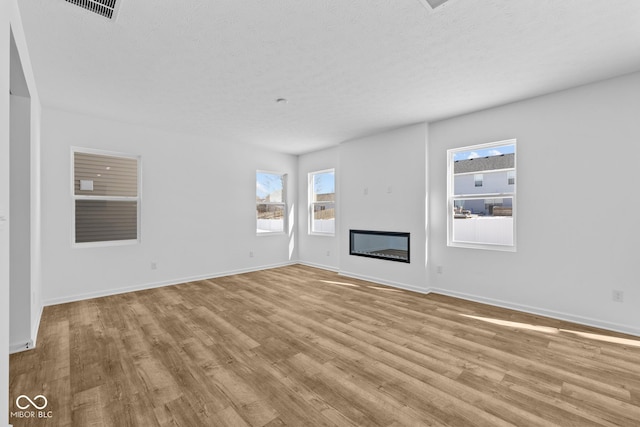 unfurnished living room featuring light wood-style floors, baseboards, a textured ceiling, and a glass covered fireplace