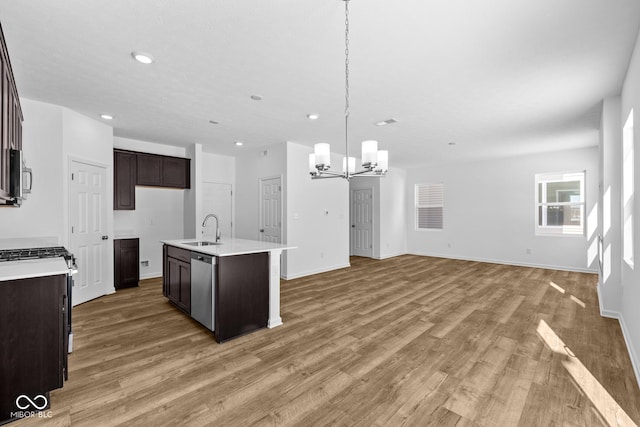 kitchen featuring stainless steel appliances, a sink, open floor plan, dark brown cabinets, and light countertops