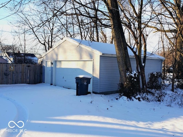 snow covered garage with a detached garage and fence