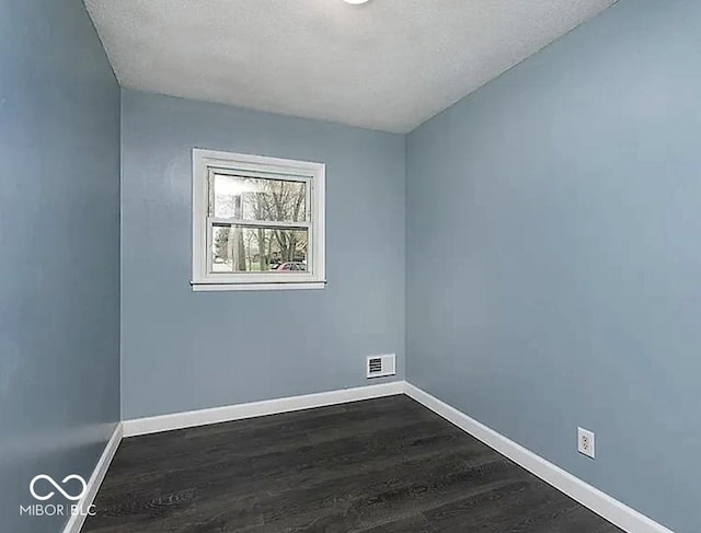 empty room featuring visible vents, baseboards, and dark wood finished floors