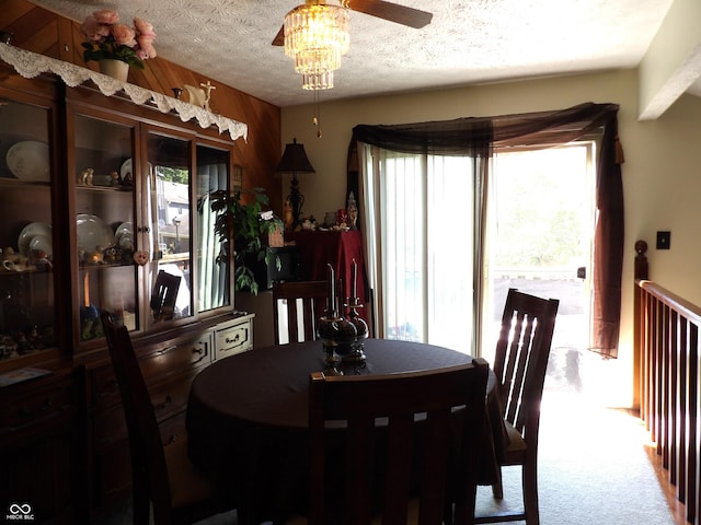 dining space featuring ceiling fan, wooden walls, a textured ceiling, and carpet flooring