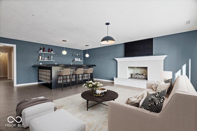 living room with a brick fireplace, hardwood / wood-style flooring, and indoor bar