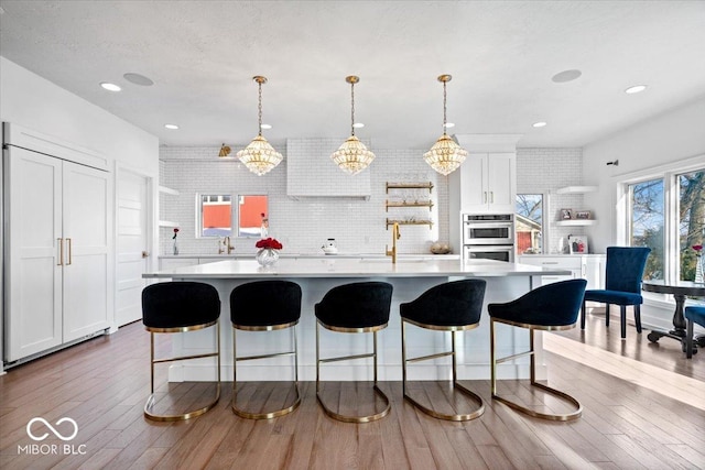 kitchen with decorative backsplash, double oven, decorative light fixtures, a center island, and white cabinetry