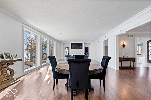 dining space with a textured ceiling, wood-type flooring, and crown molding