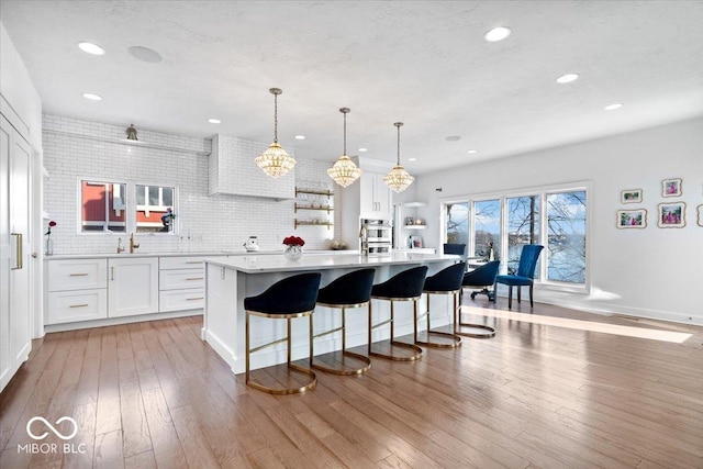 kitchen featuring a center island, white cabinets, hanging light fixtures, decorative backsplash, and a kitchen bar