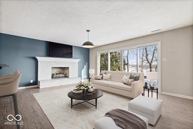 living room featuring hardwood / wood-style flooring, a textured ceiling, and a brick fireplace