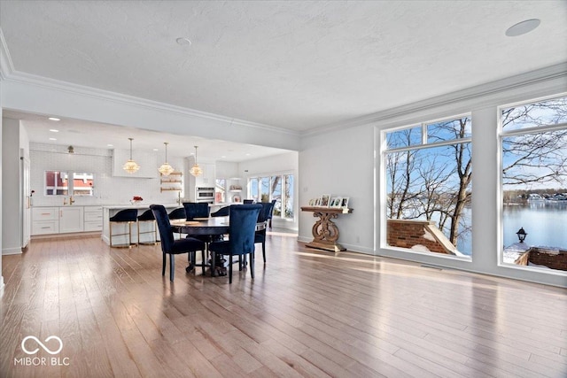 dining room featuring a textured ceiling, a water view, light wood-type flooring, and crown molding