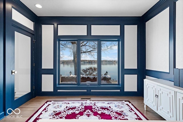 foyer entrance featuring crown molding, a water view, and wood-type flooring