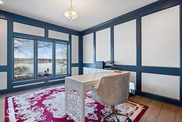 home office featuring a water view, light wood-type flooring, and crown molding