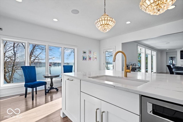 kitchen with light stone counters, sink, a water view, and a chandelier