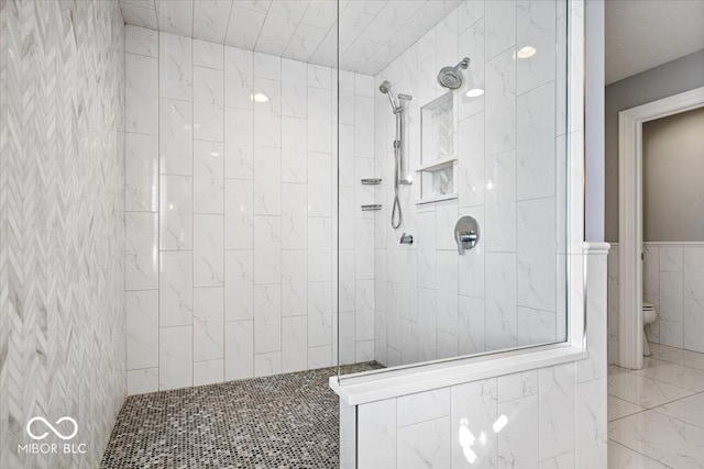 bathroom featuring a tile shower, tile walls, and toilet