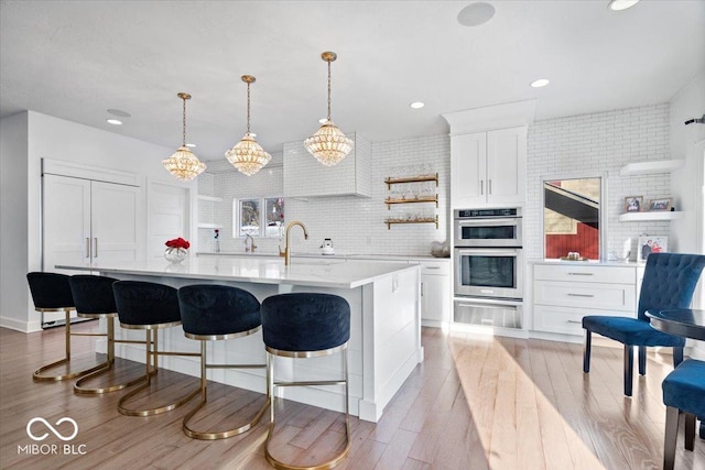 kitchen featuring tasteful backsplash, sink, decorative light fixtures, a center island with sink, and white cabinetry