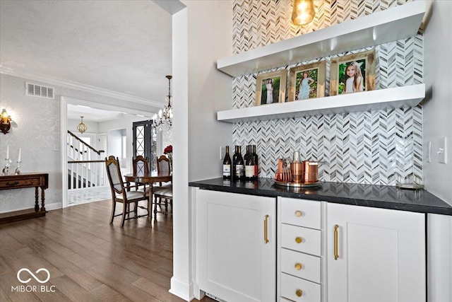 bar with backsplash, crown molding, decorative light fixtures, white cabinets, and hardwood / wood-style floors