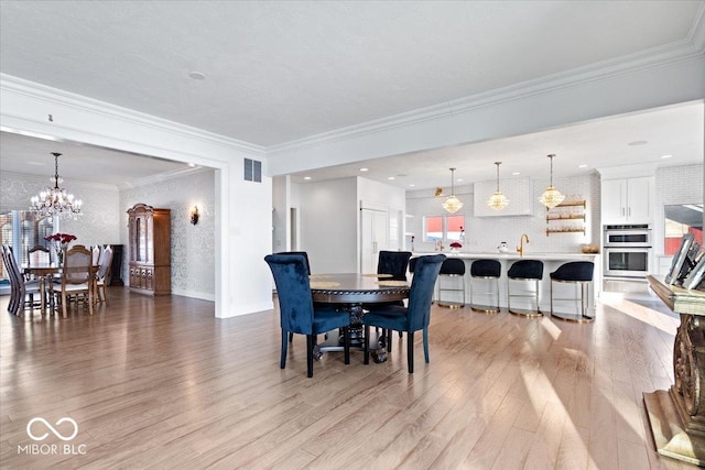 dining space featuring light hardwood / wood-style flooring, an inviting chandelier, and crown molding