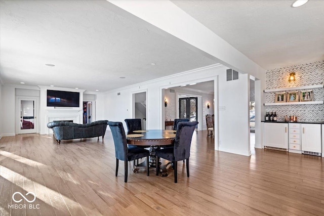 dining space featuring light hardwood / wood-style floors, crown molding, and indoor bar