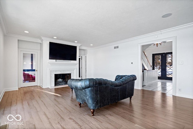 living room with a high end fireplace, french doors, light hardwood / wood-style flooring, and crown molding