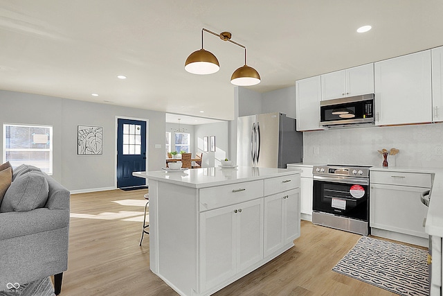 kitchen featuring a center island, white cabinets, light wood-type flooring, appliances with stainless steel finishes, and decorative light fixtures