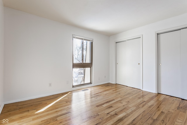 unfurnished bedroom featuring light hardwood / wood-style flooring and two closets