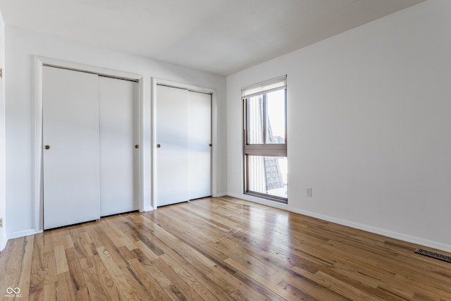 unfurnished bedroom featuring light wood-type flooring and multiple closets