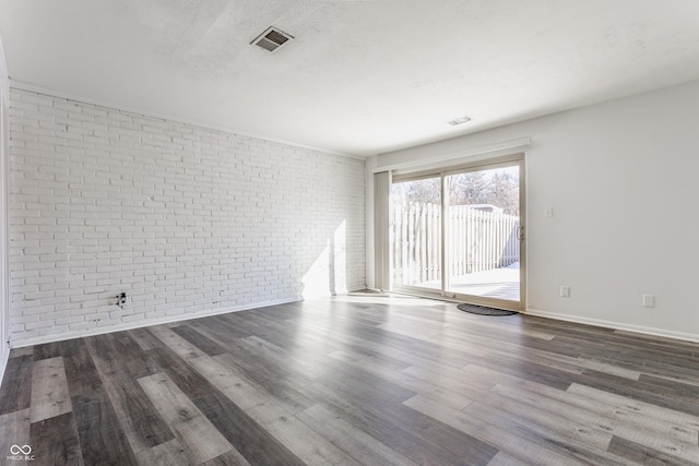 empty room featuring dark wood-type flooring and brick wall