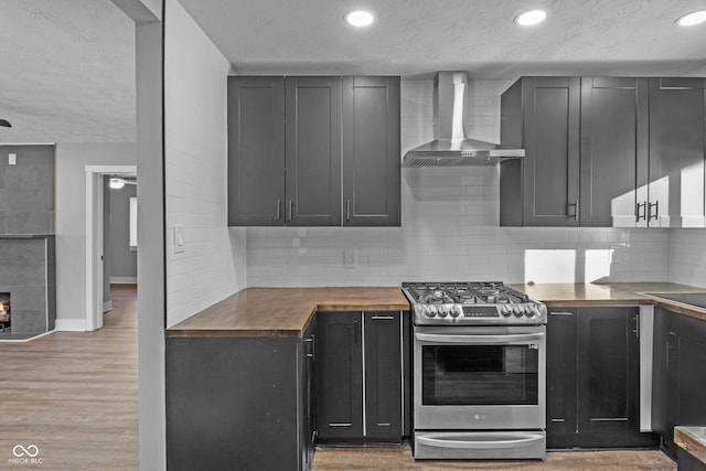 kitchen featuring wooden counters, decorative backsplash, gas range, light hardwood / wood-style flooring, and wall chimney exhaust hood