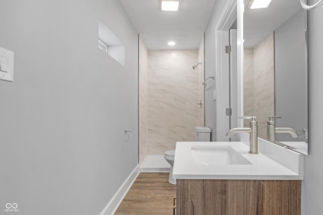 bathroom with wood-type flooring, toilet, vanity, and a tile shower