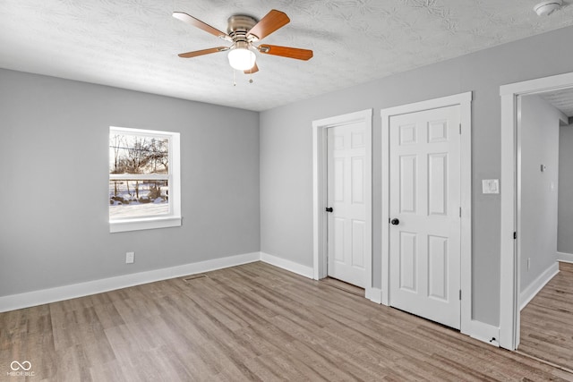 unfurnished bedroom featuring ceiling fan, two closets, a textured ceiling, and light hardwood / wood-style flooring