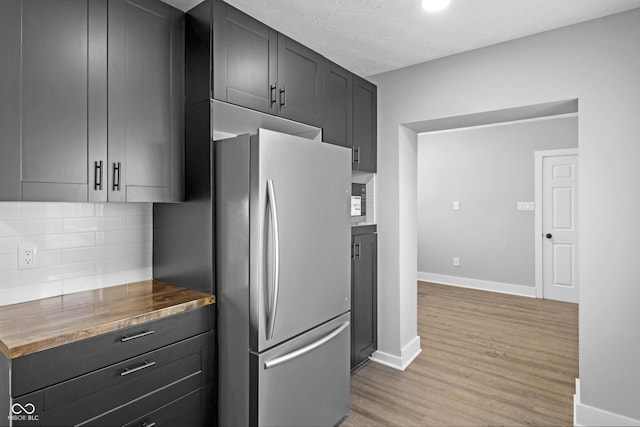 kitchen with backsplash, light hardwood / wood-style flooring, butcher block counters, and stainless steel refrigerator