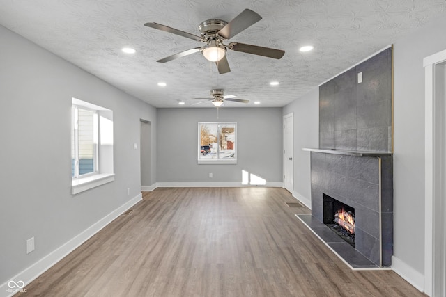 unfurnished living room with hardwood / wood-style floors, a tile fireplace, and a textured ceiling