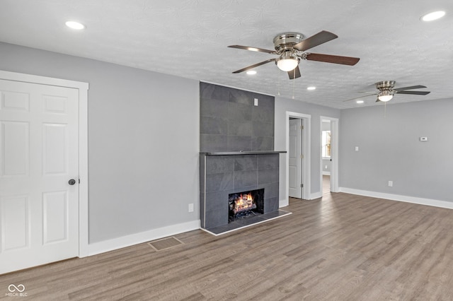 unfurnished living room featuring ceiling fan, hardwood / wood-style floors, a fireplace, and a textured ceiling