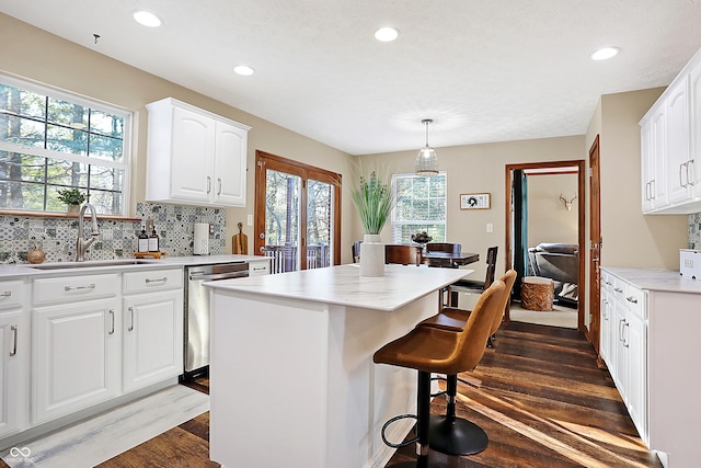 kitchen featuring white cabinetry, dishwasher, sink, hanging light fixtures, and a kitchen island