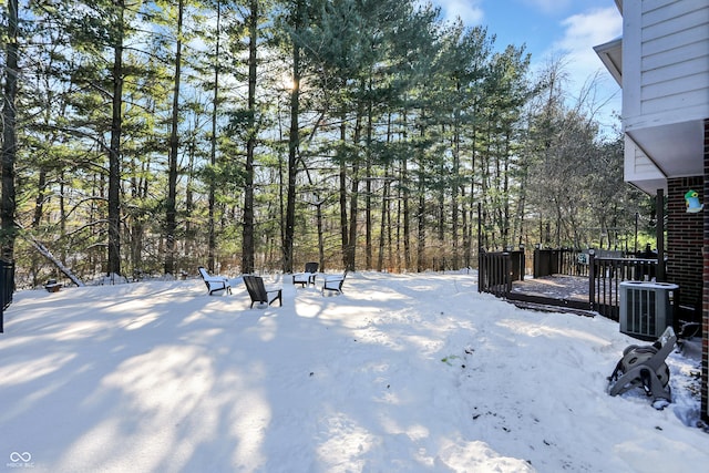 snowy yard with central AC and a wooden deck