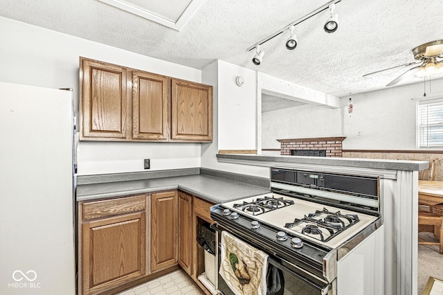 kitchen with ceiling fan, white fridge, range with gas stovetop, and a textured ceiling