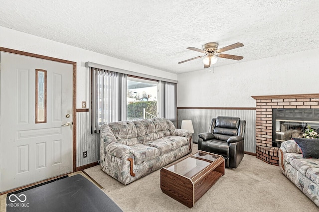 living room with light carpet, a brick fireplace, a textured ceiling, ceiling fan, and wood walls