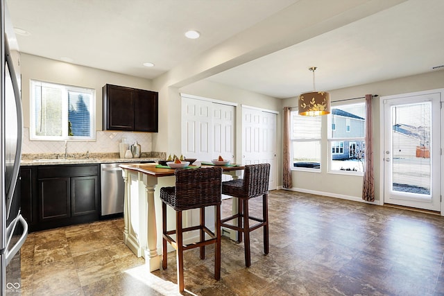 kitchen with sink, dark brown cabinets, hanging light fixtures, a kitchen breakfast bar, and backsplash