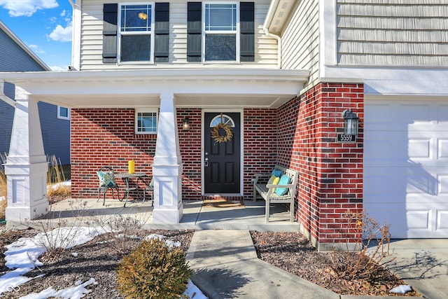 snow covered property entrance featuring a porch and a garage