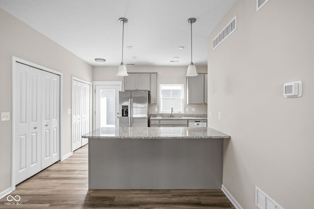 kitchen featuring light stone countertops, kitchen peninsula, stainless steel appliances, sink, and hanging light fixtures