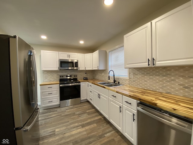 kitchen with butcher block counters, white cabinetry, sink, and stainless steel appliances