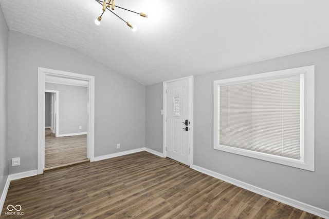 spare room with dark wood-type flooring, lofted ceiling, and a notable chandelier