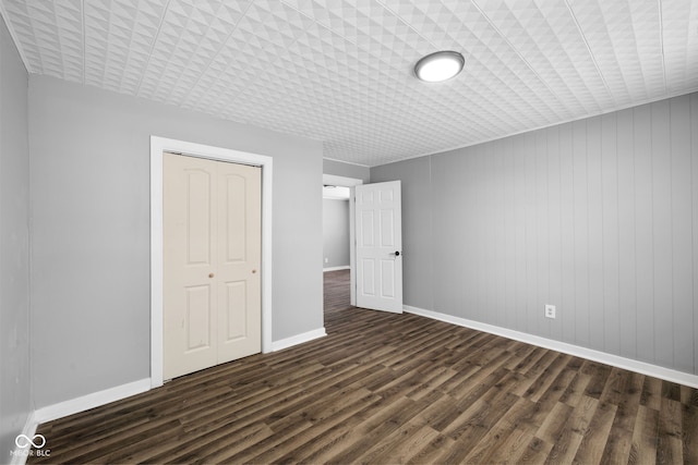 unfurnished bedroom featuring dark hardwood / wood-style flooring, wood walls, and a closet