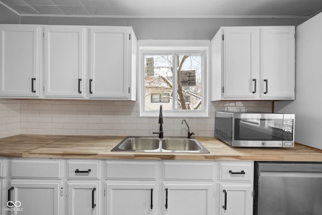 kitchen featuring sink, decorative backsplash, appliances with stainless steel finishes, white cabinetry, and butcher block counters