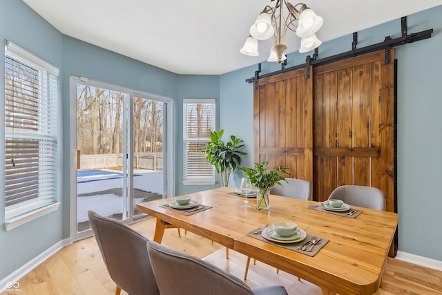 dining space with a barn door, a chandelier, and light hardwood / wood-style flooring