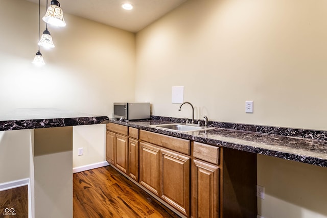 kitchen featuring brown cabinetry, dark wood-style flooring, a sink, pendant lighting, and stainless steel microwave