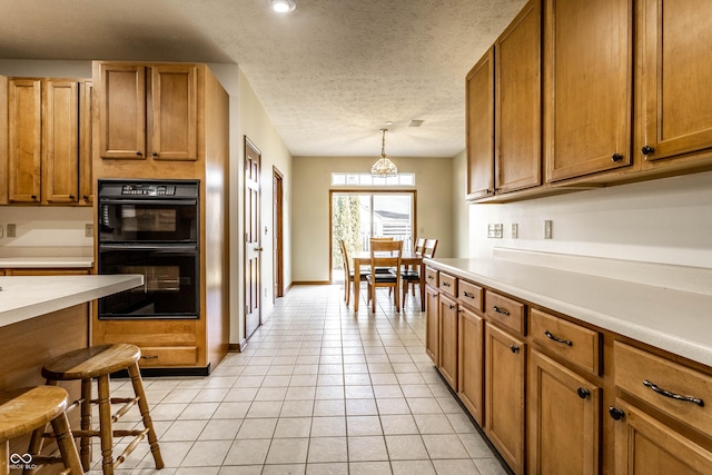 kitchen with brown cabinetry, light countertops, light tile patterned flooring, a textured ceiling, and dobule oven black