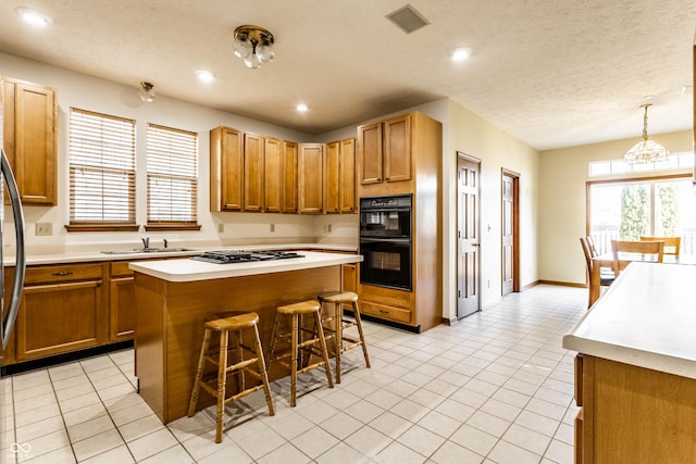 kitchen with visible vents, a kitchen island, light countertops, a kitchen breakfast bar, and black appliances