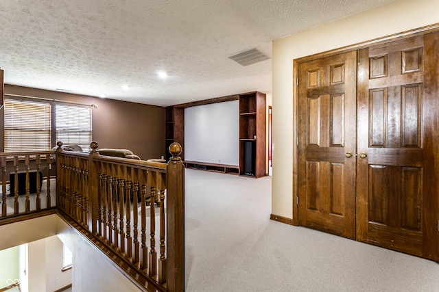 hallway with visible vents, an upstairs landing, a textured ceiling, carpet flooring, and baseboards