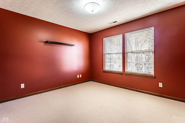 empty room with a textured ceiling, carpet, visible vents, and baseboards