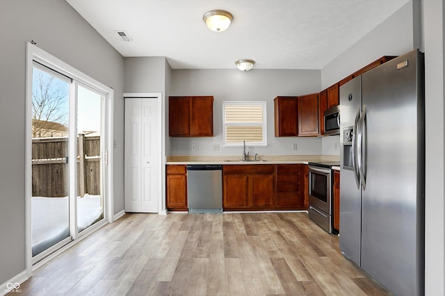 kitchen with appliances with stainless steel finishes, sink, and light hardwood / wood-style floors