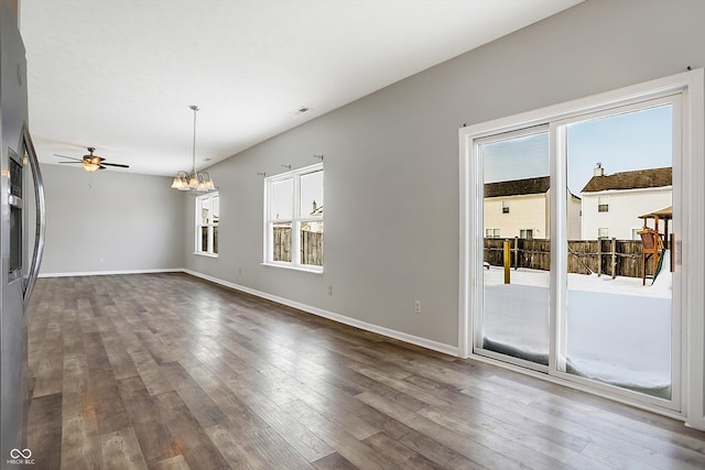 unfurnished living room with ceiling fan with notable chandelier, a wealth of natural light, and hardwood / wood-style floors