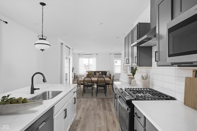 kitchen with sink, wall chimney exhaust hood, stainless steel appliances, light hardwood / wood-style floors, and decorative light fixtures